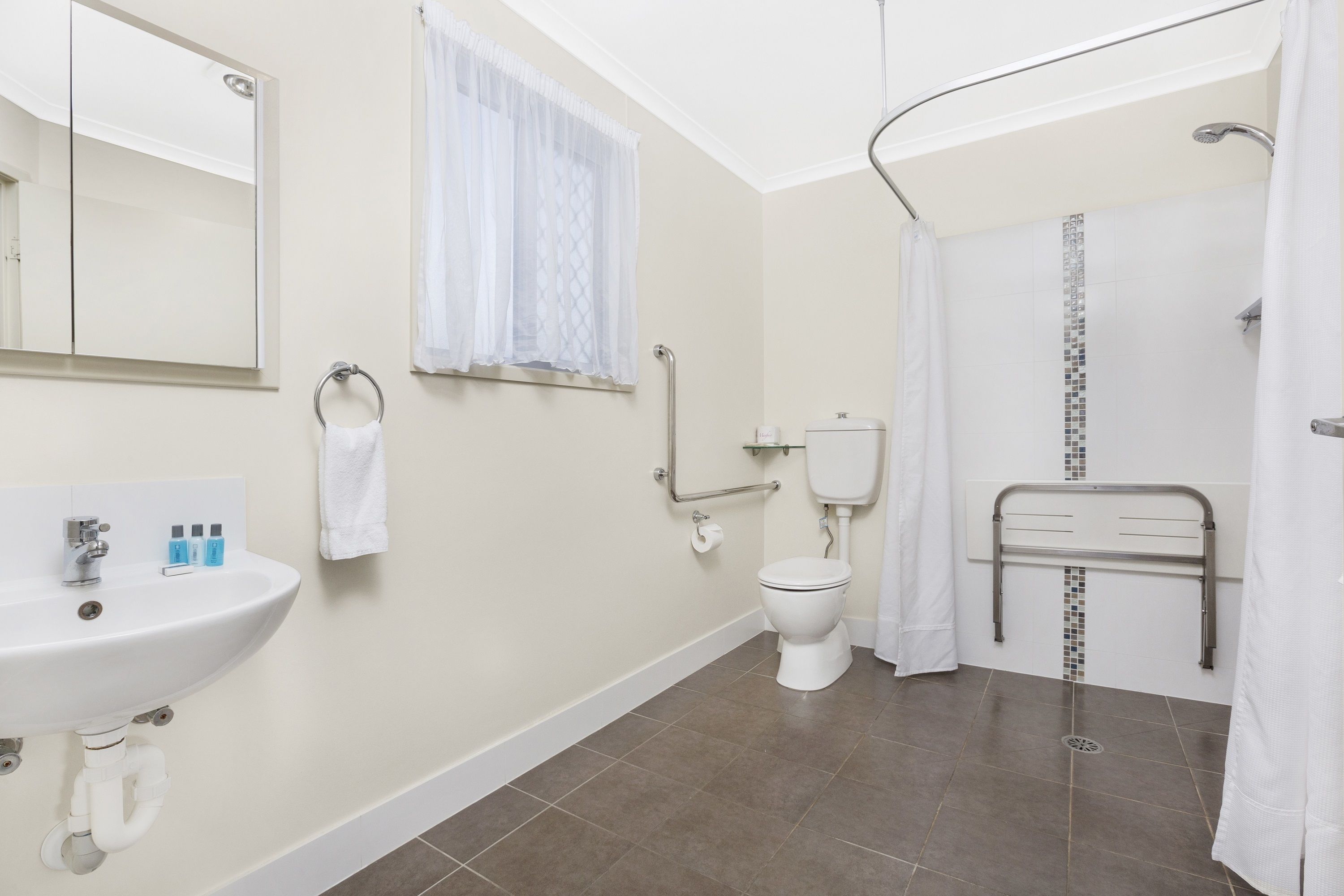 A bathroom with a sink, toilet, shower, and a handrail.