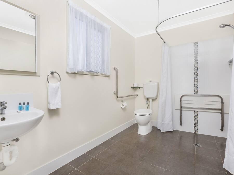 A bathroom with a sink, toilet, shower, and a handrail.