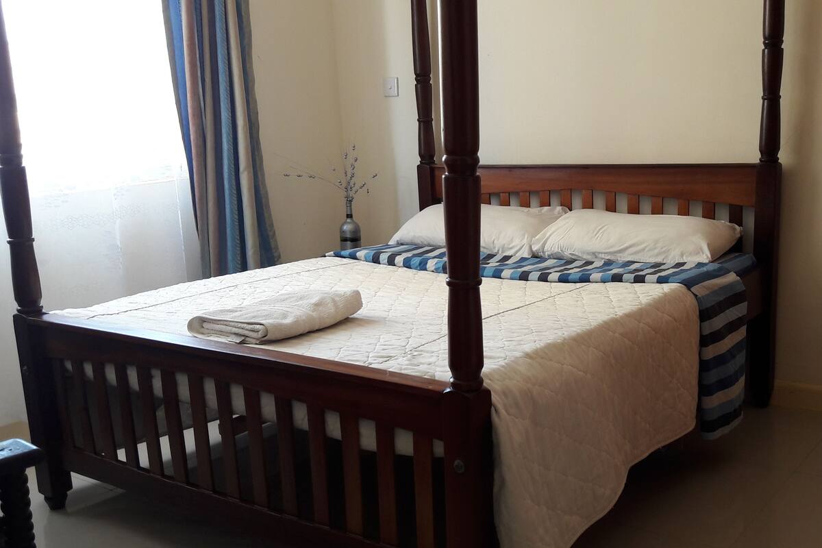 A four-poster bed with a quilted bedspread and a folded towel on the footboard.