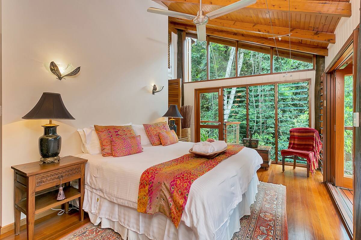 A bedroom with a large bed, wooden headboard, and a view of the outdoors.