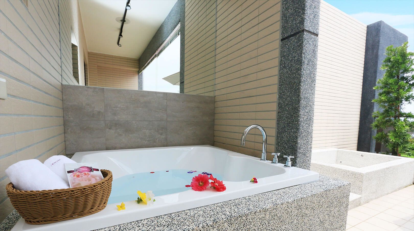 Une salle de bain moderne avec une baignoire sur pieds, un panier en osier rempli de serviettes et un petit arrangement floral.