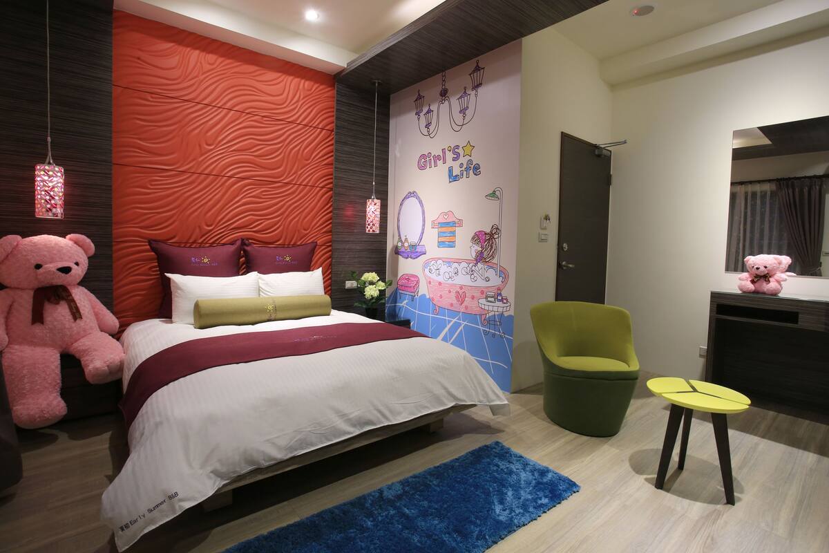 Un dormitorio con una cama, una silla verde, una mesita, un peluche y una pared con un mural.