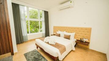 A hotel room with a large bed, a wooden headboard, a nightstand, and a window with curtains.