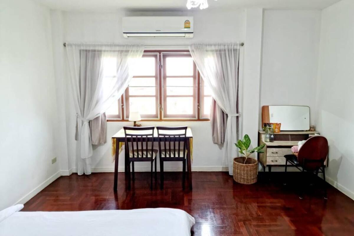 A room with a bed, a desk with a chair, a computer, and a window with curtains.
