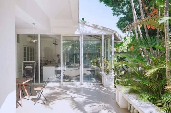 A modern house with a glass door leading to a patio area, surrounded by lush greenery.