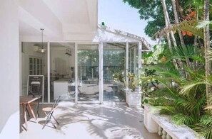 A modern house with a glass door leading to a patio area, surrounded by lush greenery.
