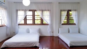 A room with two single beds, white bedding, and large windows with white curtains.