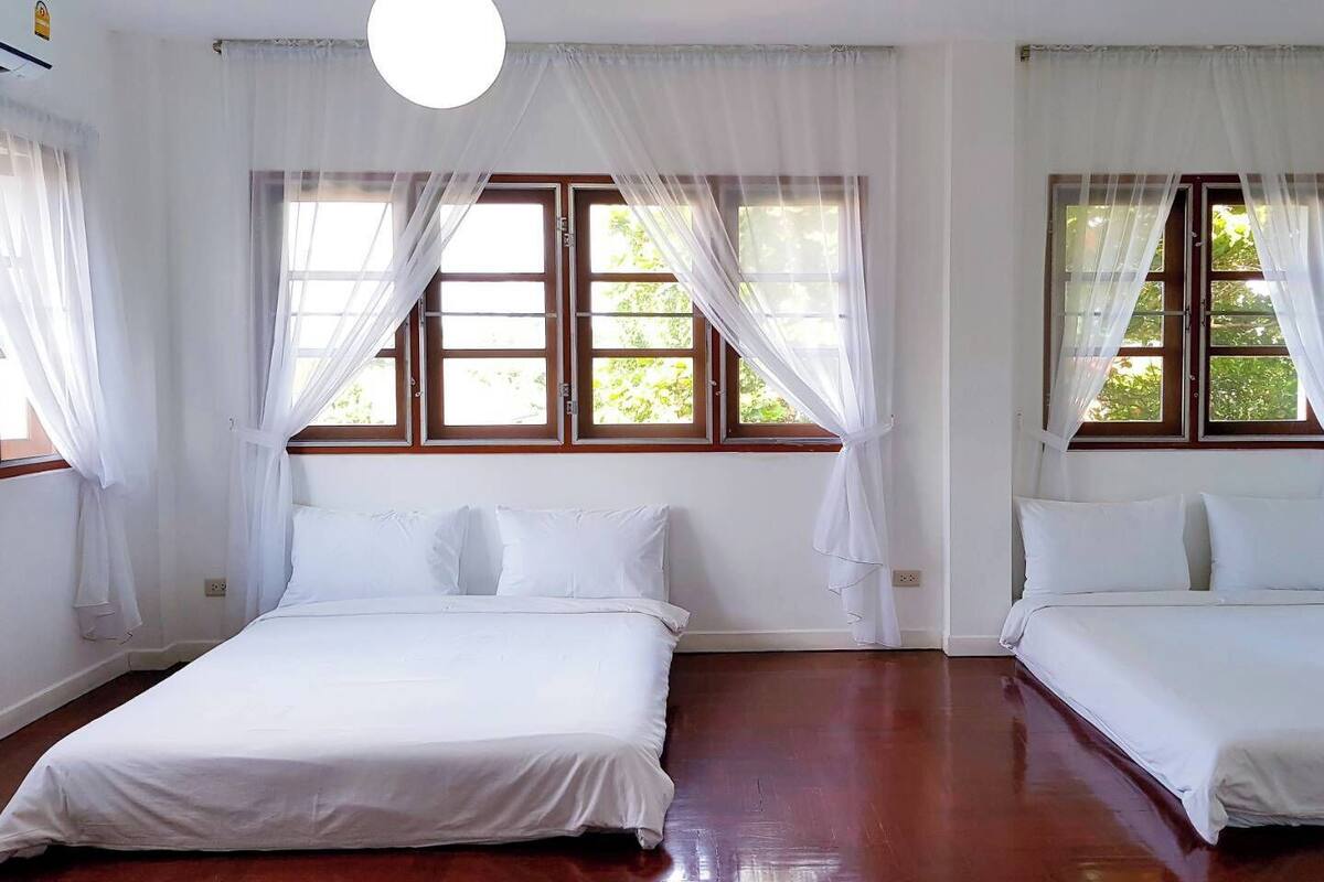 A room with two single beds, white bedding, and large windows with white curtains.