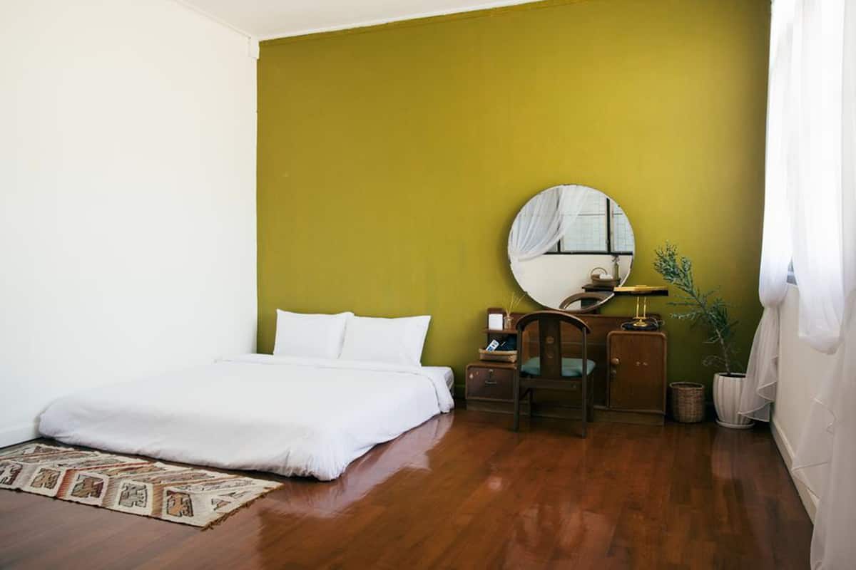 A bedroom with a large bed, a round mirror, a nightstand, a chair, and a potted plant.