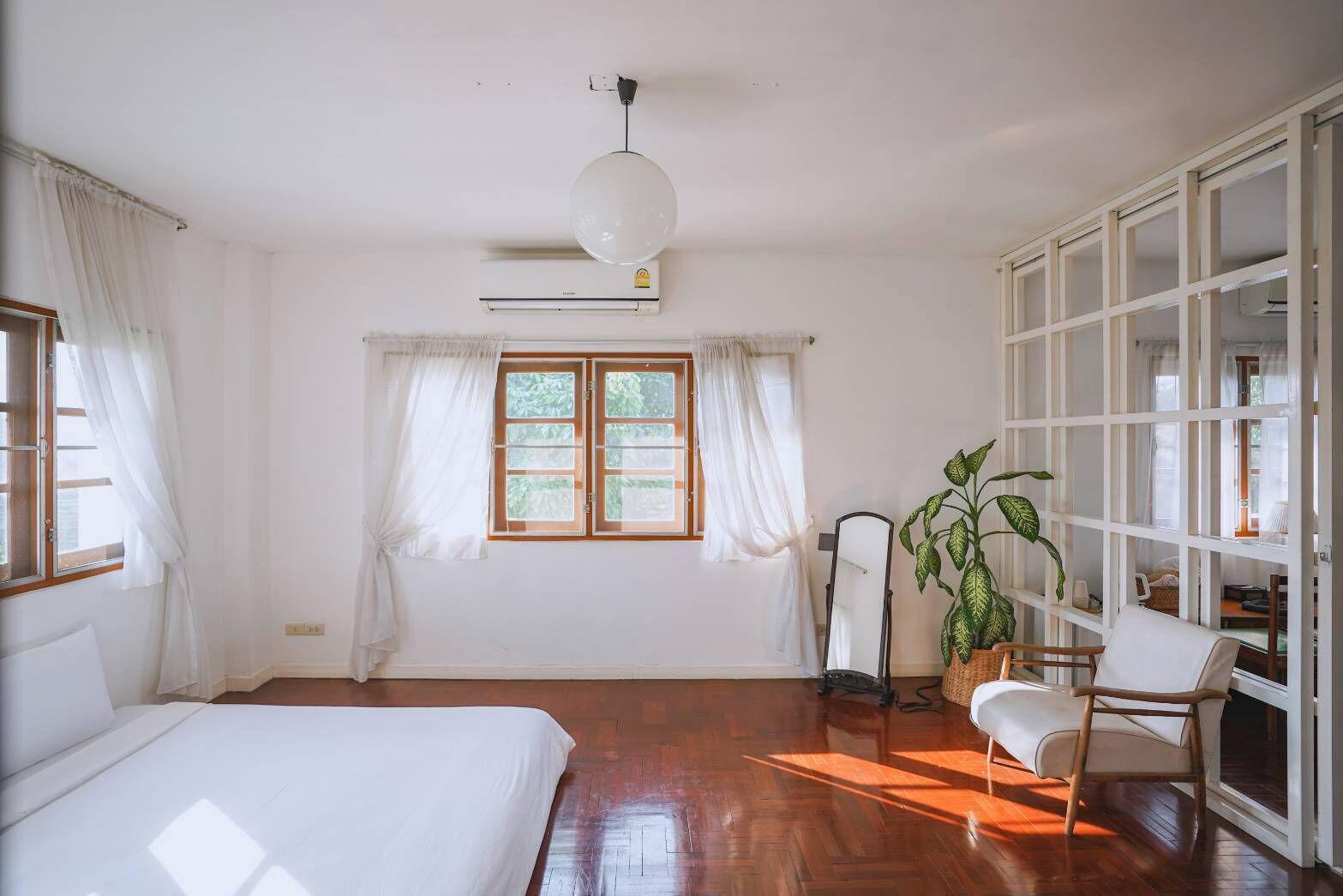 Una habitación con una cama, una silla, una planta en maceta, un espejo y un armario.