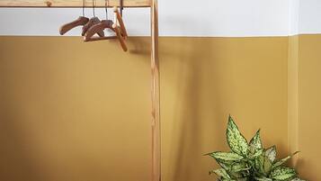 A wooden drying rack against a wall with a yellow and white color scheme, and a potted plant with variegated leaves.