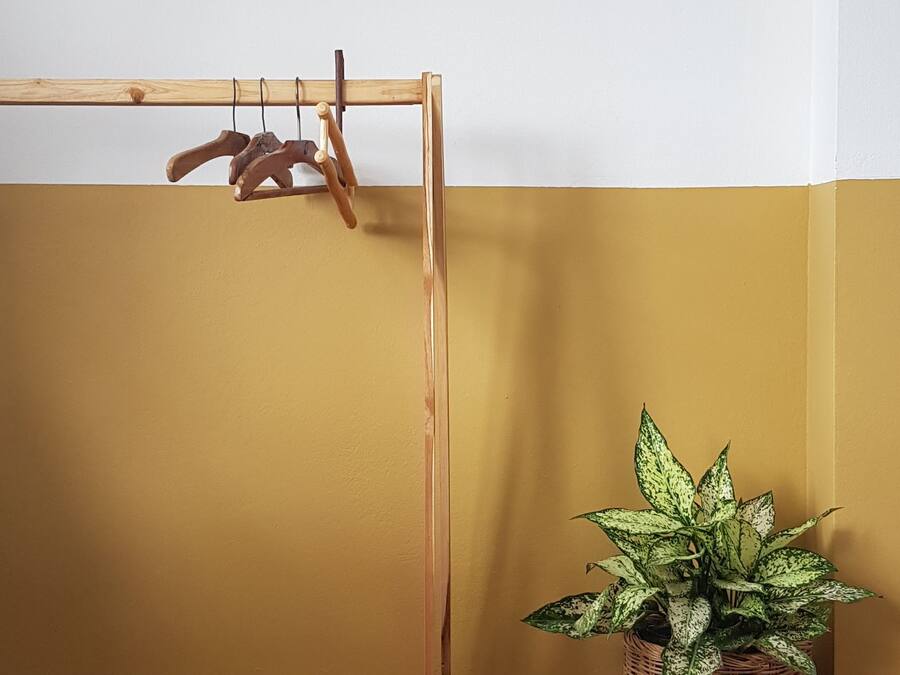 A wooden drying rack against a wall with a yellow and white color scheme, and a potted plant with variegated leaves.