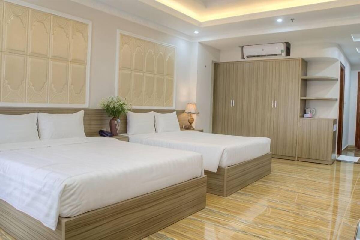 A hotel room with two beds, a wardrobe, a desk, and a plant.