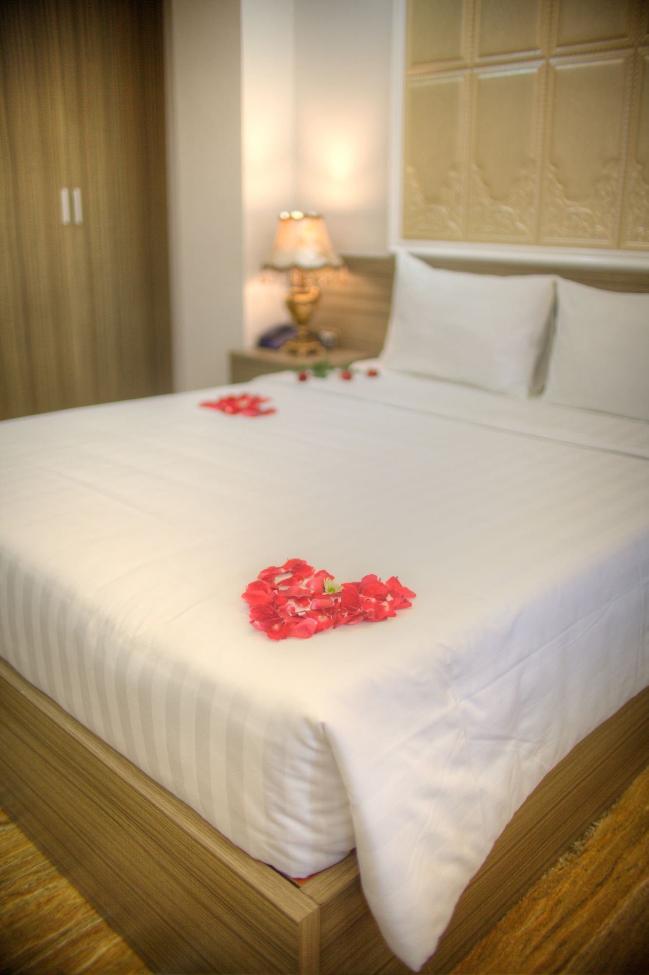 Una habitación de hotel con una cama bien hecha, una mesita de noche con lámpara y un cabecero de madera.