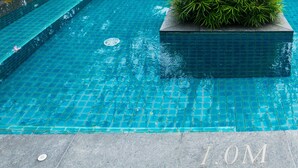 A rectangular swimming pool with blue tiles and a central planter with green foliage.