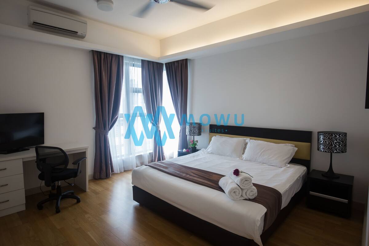 Une chambre d’hôtel comprenant un lit, un bureau avec une chaise, une télévision, une table de chevet avec une lampe et une fenêtre avec des rideaux.
