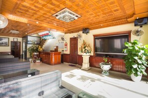 Experience the traditional charm of our lobby, featuring a geometric ceiling, comfortable seating areas, and a reception desk with a beautiful floral arrangement.