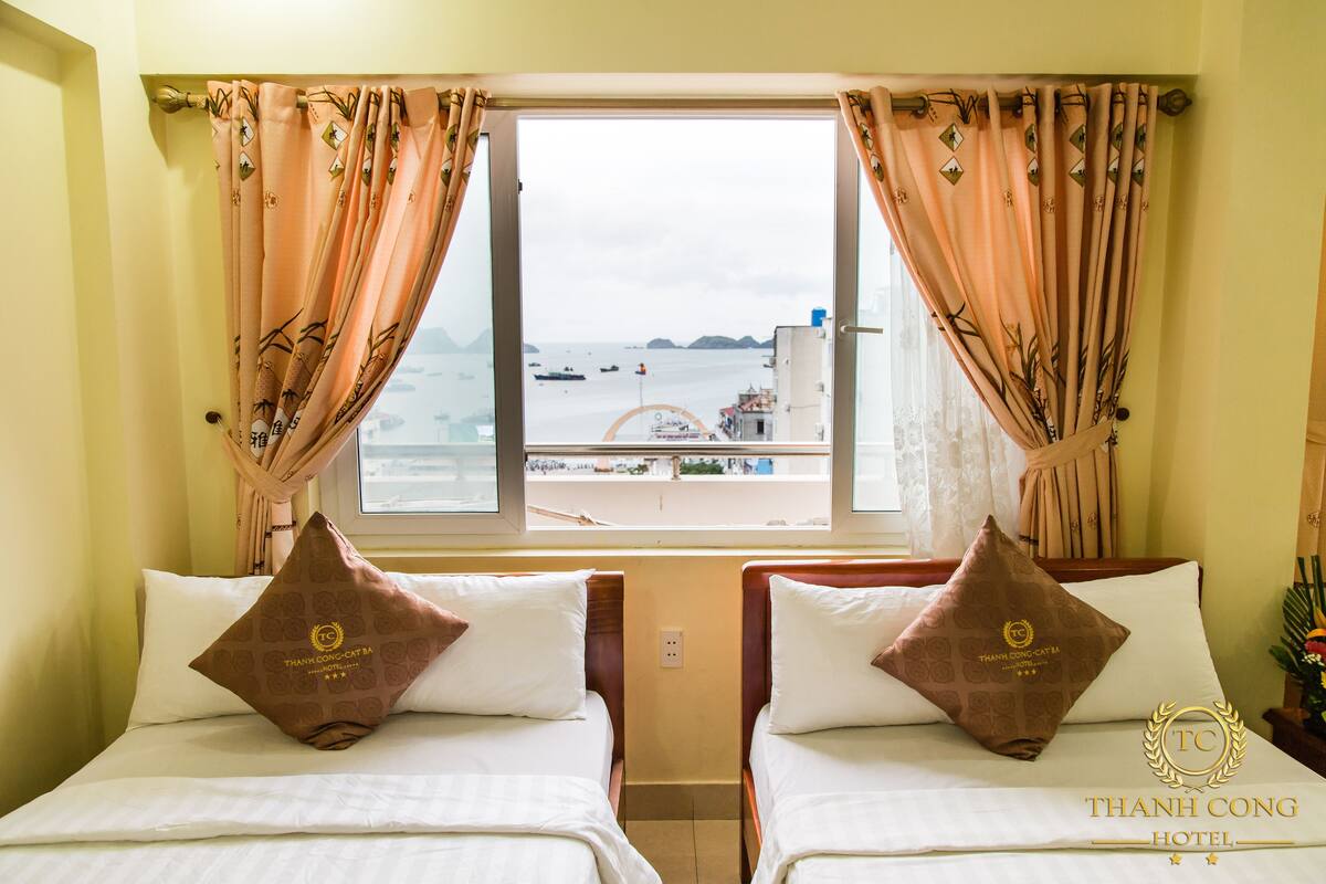 A hotel room with two beds, a window with a view of the sea, and a logo on the pillows.
