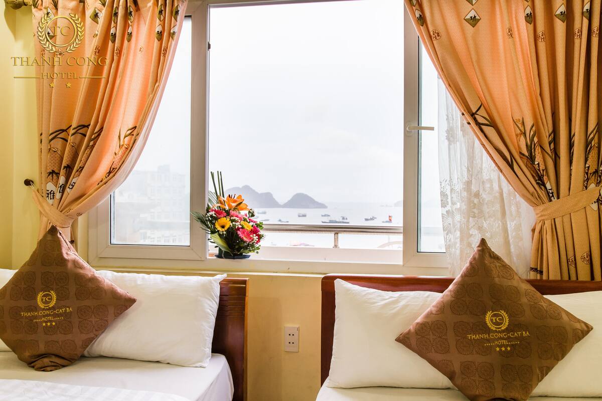A hotel room with two beds, a window with curtains, and a view of the sea.