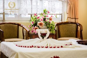 A hotel room with a bed, two chairs, a table with a vase of flowers, and a window with curtains.