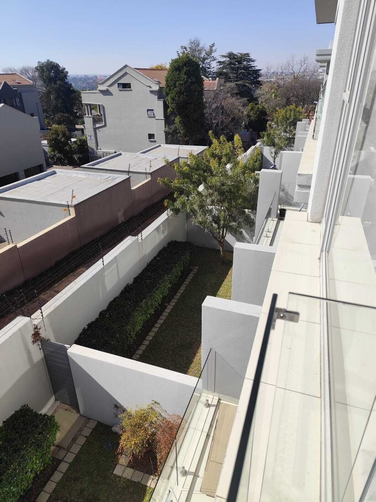 Un bâtiment moderne doté d’un toit plat, de murs blancs et d’un petit espace jardin agrémenté d’un arbre et d’arbustes.