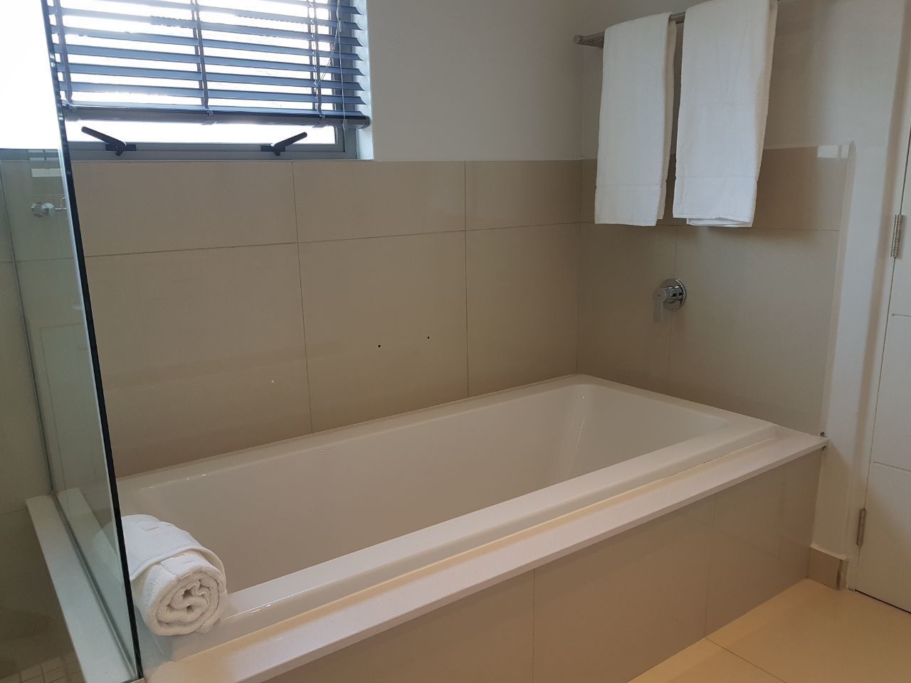 A bathroom with a bathtub, a glass shower enclosure, and two white towels hanging on the wall.