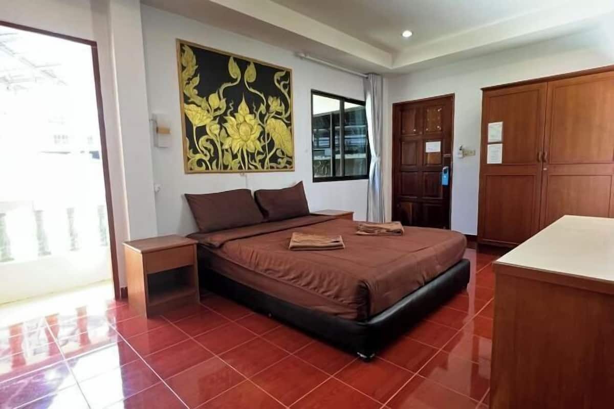A bedroom with a bed, a nightstand, a wooden wardrobe, a window, and a wall decoration.