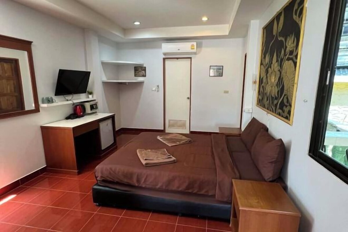 Una habitación de hotel compacta con cama, escritorio, televisión y ventana.