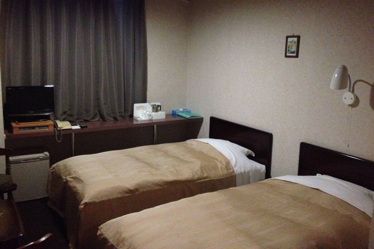 Ein Hotelzimmer mit zwei Betten, einem Schreibtisch mit Fernseher, Telefon und einem kleinen Tisch mit Kaffeemaschine.