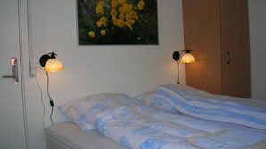 Un dormitorio con una cama, dos lámparas adosadas a la pared, un armario de madera y un cuadro enmarcado con flores amarillas.