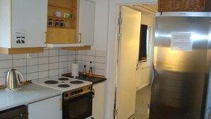 Una cocina compacta con estufa, horno y refrigerador. Hay un estante pequeño con utensilios de cocina y una tetera en la encimera.
