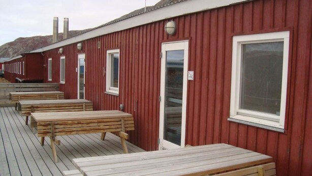 Una hilera de cabañas rojas de madera con ventanas y puertas enmarcadas en blanco, cada una con un ventanal y una puerta.