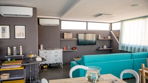 Una sala de estar moderna con un sofá azul verdoso, una mesa de comedor de madera y una cocina con un carrito y electrodomésticos.