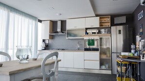 Una cocina moderna con armarios blancos, un refrigerador de acero inoxidable y una zona de comedor con una mesa y sillas de madera.