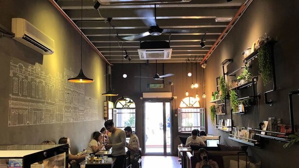 L’intérieur d’un restaurant, avec des tables, des chaises, des luminaires suspendus et une fresque murale.