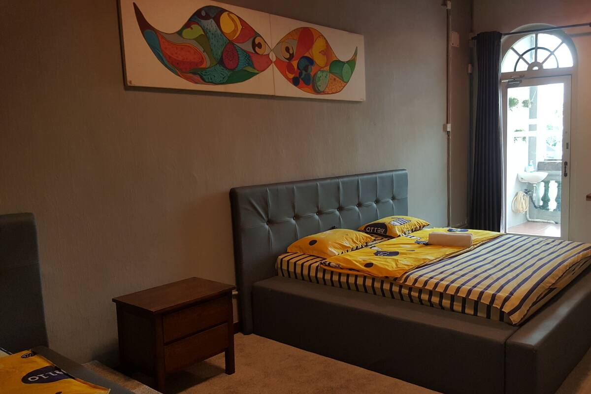 A bedroom with a tufted headboard bed, striped bedding, a small bedside table, and a colorful abstract painting on the wall.