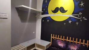 Une chambre d’enfant avec une fresque murale sur le thème de la nuit, un petit lit en bois et une étagère blanche.