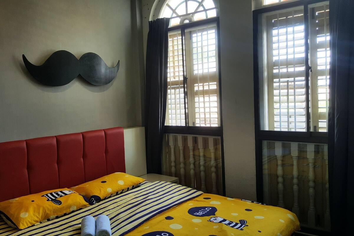 A bed with a red headboard, striped bedding, and two yellow pillows with a mustache design.