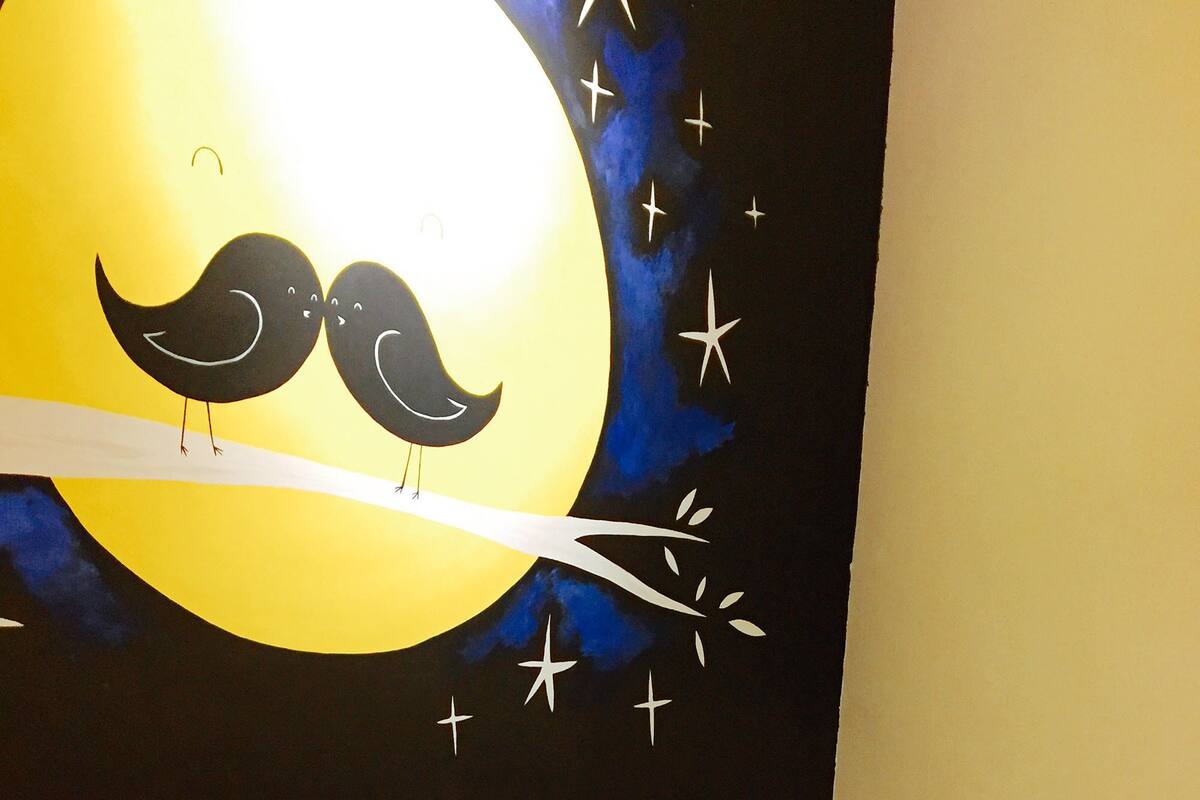 A bedroom with a bed featuring a floral bedspread, a night sky mural with birds and stars, and a wooden headboard.