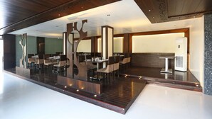 A modern restaurant with a central bar area, multiple dining tables, and a polished wooden floor. - Hotel Satyan Inn (Rahata)