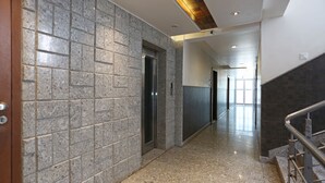 A hallway with a marble floor, a wooden door on the left, and a metal railing on the right. - Hotel Satyan Inn (Rahata)