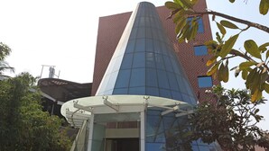 A modern building with a glass facade and a conical roof structure. - Hotel Satyan Inn (Rahata)