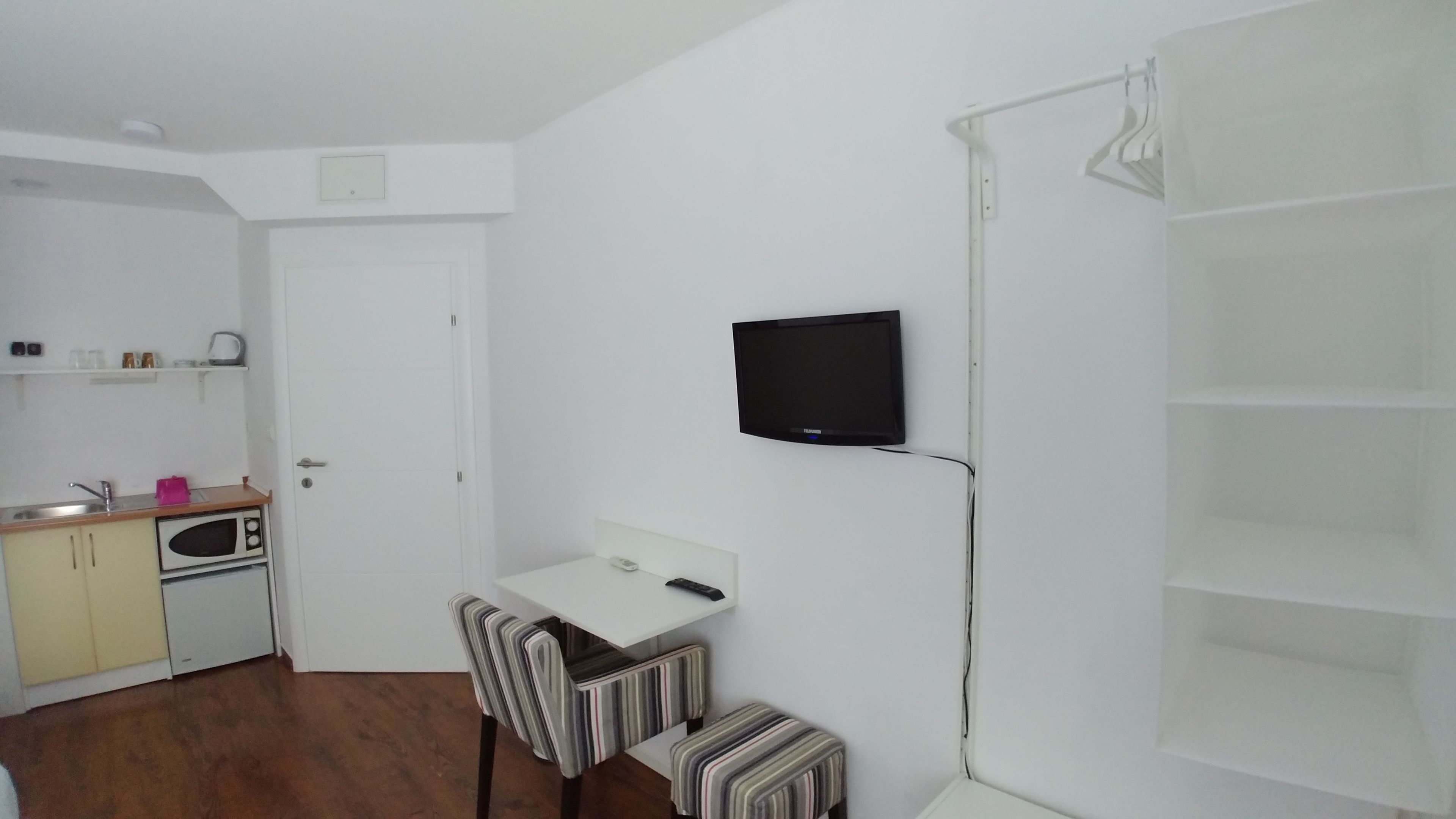 A compact room with a kitchenette, a TV mounted on the wall, and a small seating area.