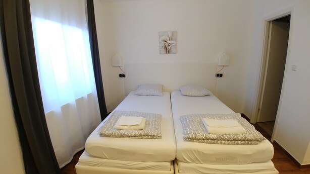 Ein Doppelzimmer mit zwei Betten, jeweils mit gemusterten Bettwäsche und Kissen, einem kleinen Gemälde an der Wand und einer Tür zu einem weiteren Raum.