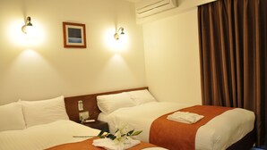 Habitación de hotel con dos camas, cada una con sábanas blancas y mantas marrones, una mesita de noche con teléfono y luces fijadas a la pared.