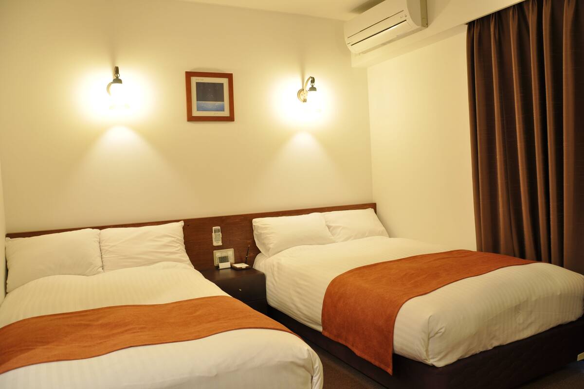 Una habitación de hotel con dos camas, una mesita de noche, un cuadro enmarcado y un equipo de aire acondicionado.