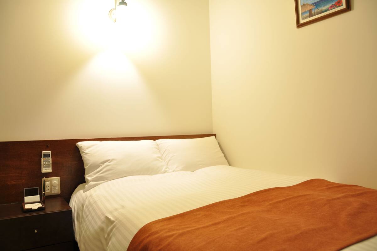 Habitación de hotel con cama, mesita de noche, teléfono y un cuadro en la pared.