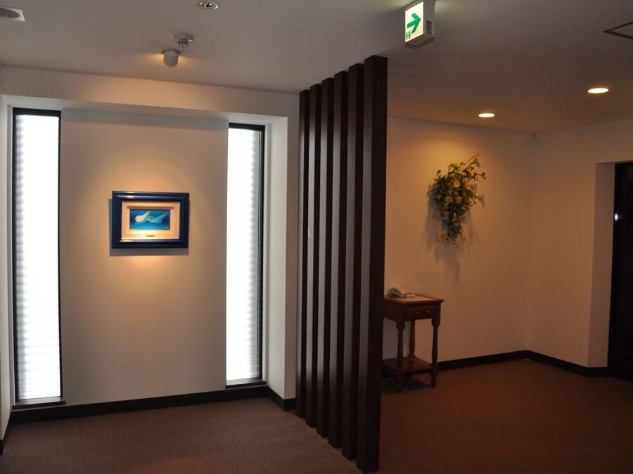 A hallway with a framed picture on the wall, a plant, and a door with an exit sign.