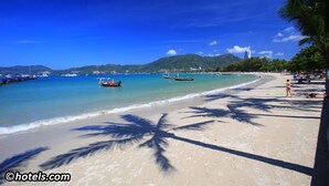 A beach with clear blue water, boats, and palm trees. - 77 Bangla Hotel (Patong)