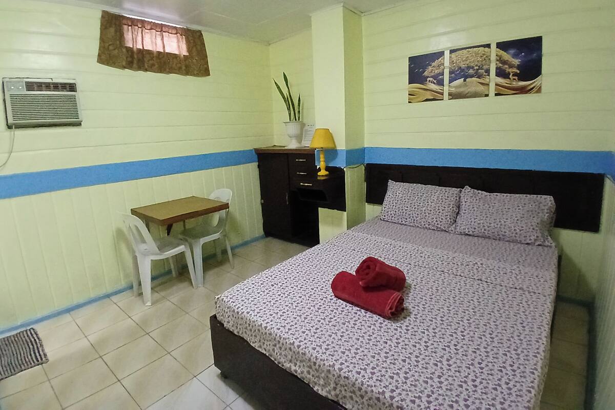 A room with a bed, a desk, a chair, a window with curtains, a wall-mounted air conditioner, and a wall decoration.